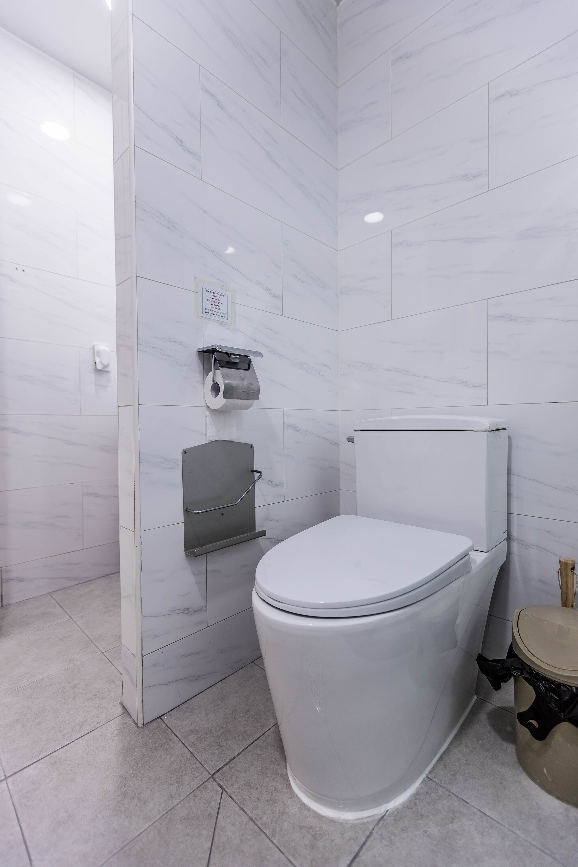 A modern bathroom with a white toilet, a paper towel dispenser, and a trash bin.