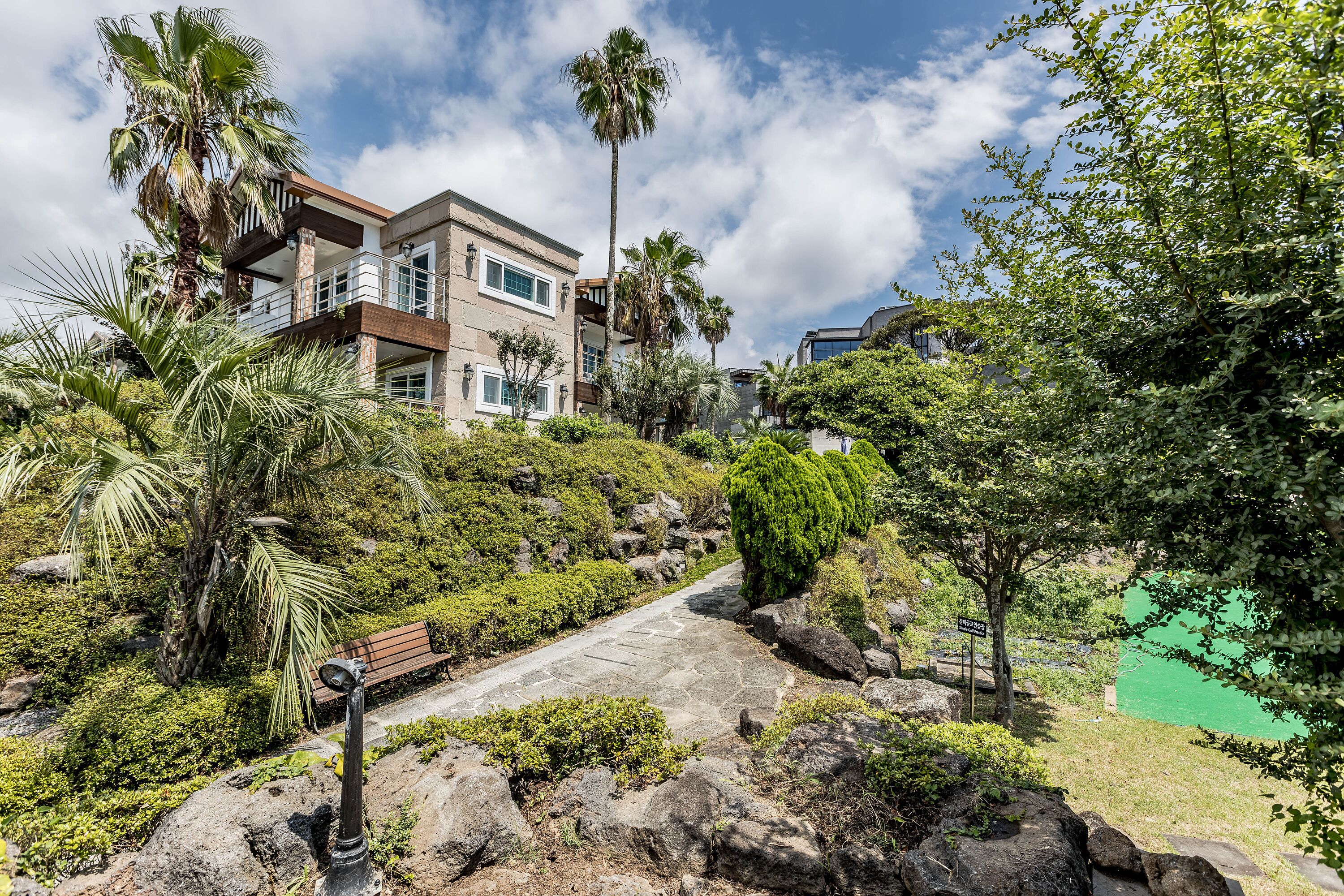 A multi-story building with a balcony, surrounded by lush greenery and palm trees.