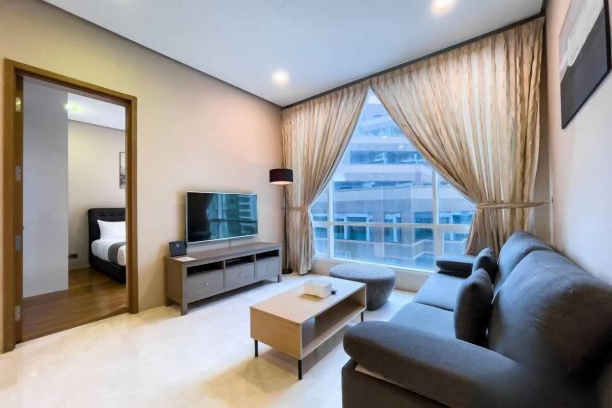 A modern living room with a sofa, a coffee table, a TV, and a large window with curtains.