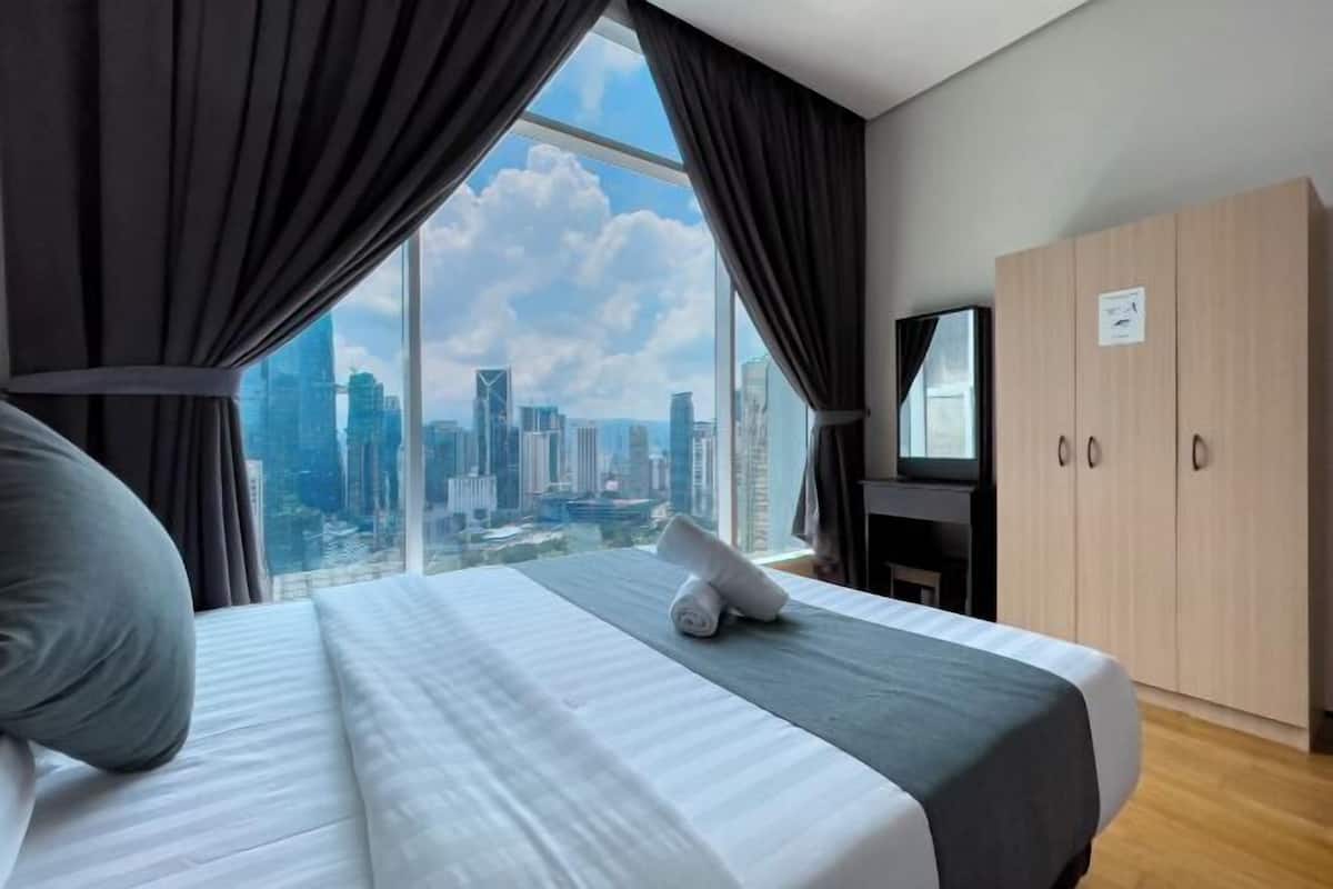 A hotel room with a large bed, a TV, a wardrobe, and a view of a cityscape.