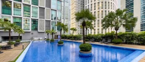 Una piscina con cubierta de madera, rodeada de palmeras y edificios modernos.