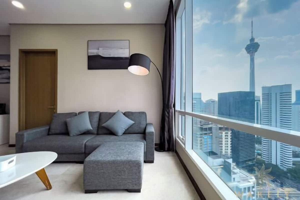 A modern living room with a grey sofa, a small table, and a large window offering a city view.