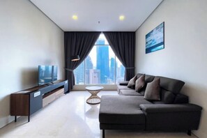 A modern living room with a sofa, TV, and a view of the cityscape through large windows.