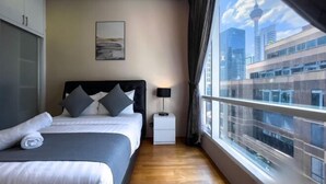 Een moderne hotelkamer met een groot bed, een nachtkastje, een lamp en uitzicht op een stadslandschap door een groot raam.