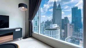 Een moderne kamer met een groot raam, een flatscreen televisie, een zwarte vloerlamp en een houten bijzettafeltje.