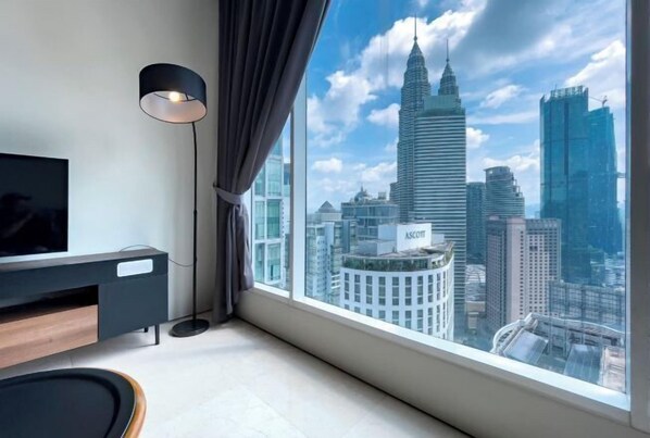 A modern room with a large window, a flat-screen TV, a black floor lamp, and a wooden side table.