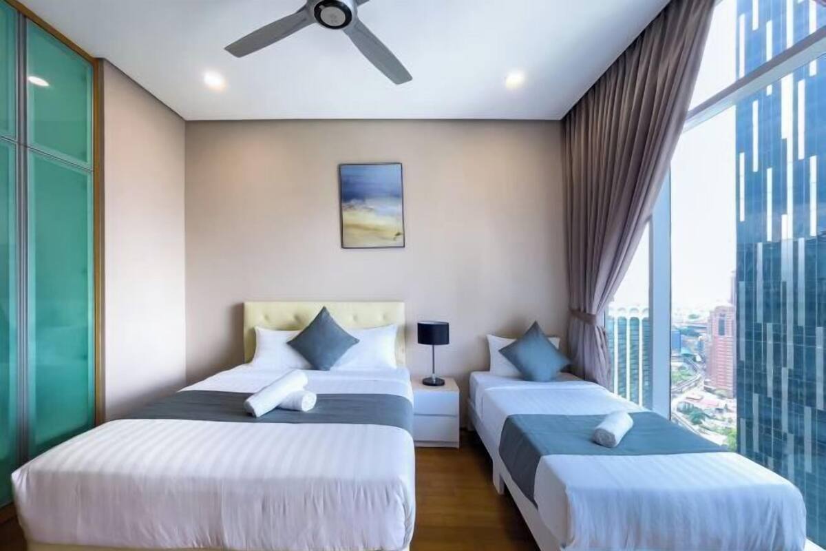 A hotel room with two beds, a ceiling fan, a nightstand, a lamp, and a painting on the wall.