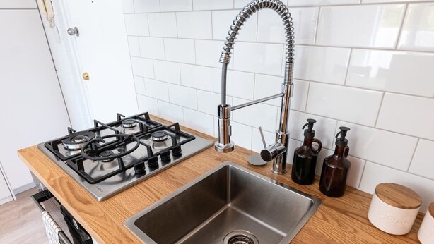 Una cocina con un lavamanos de acero inoxidable, una estufa a gas y encimeras de madera.