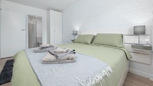 Un dormitorio moderno con una cama bien hecha, una mesita de noche con lámpara y una pared con diseño de ladrillo.