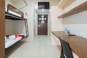 Habitación de hotel con literas, escritorio, silla, televisor y puerta con un cartel.