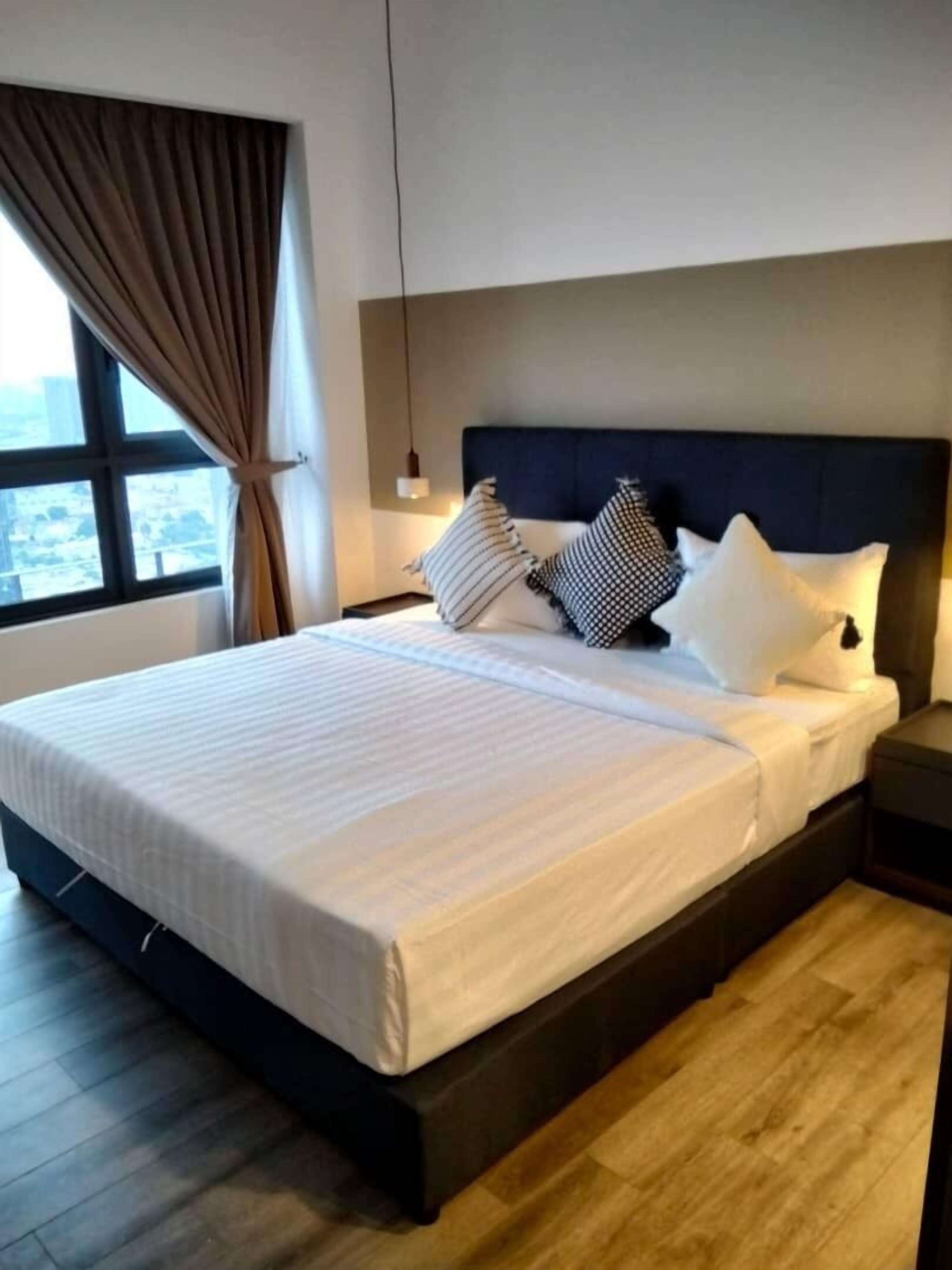 Habitación de hotel moderna con una cama grande, cabecera oscura y vistas a través de una ventana con cortinas.