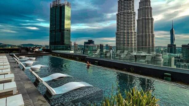 A rooftop pool with lounge chairs and a view of the Petronas Twin Towers.