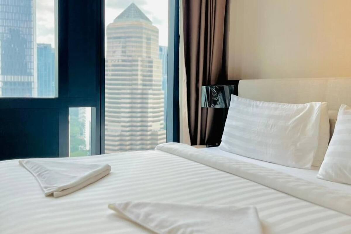 A hotel room with a large bed, a view of a cityscape, and a window with curtains.