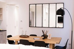 A dining area with a wooden table, black chairs, a black pendant lamp, and a large mirror on the wall.
