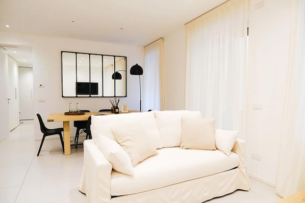 A modern living room with a white sofa, a dining table, and a large mirror on the wall.