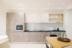 A modern kitchen with grey cabinets, a built-in oven, a sink, and a dining area with a wooden table.