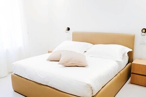 Una cama con cabecera color beige, ropa de cama blanca y dos mesitas de noche con lámparas.