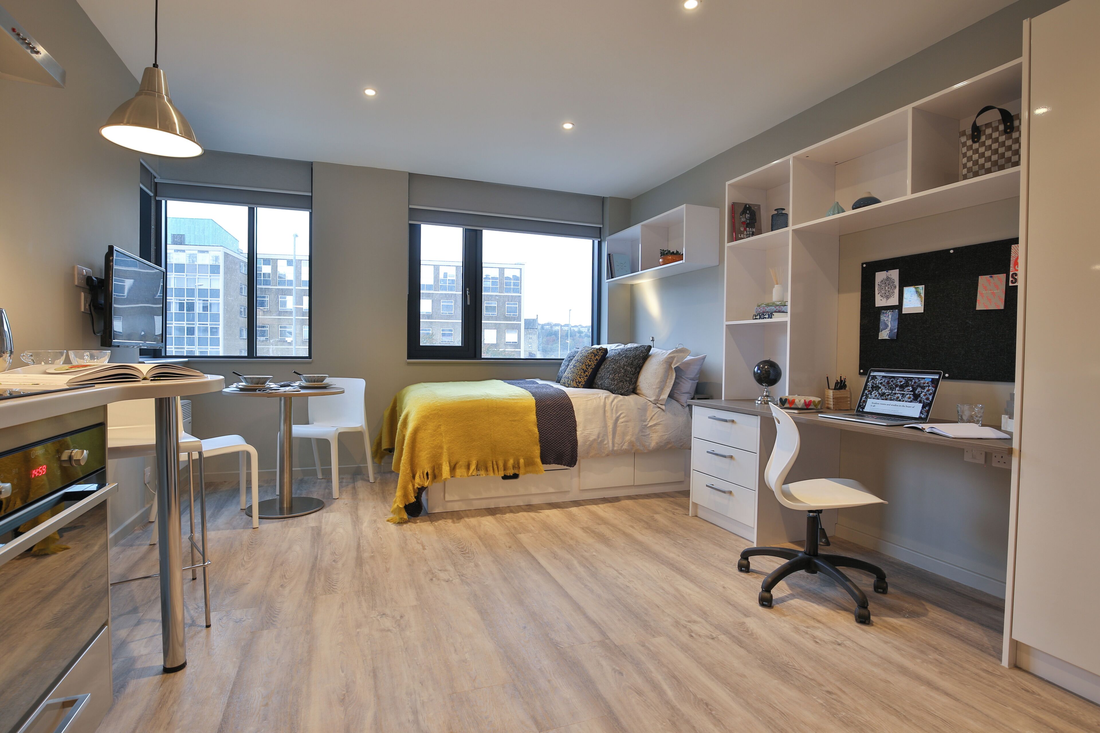 A modern bedroom with a bed, desk, and chair, a window with a city view, and a bookshelf.
