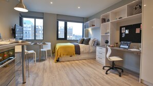 A modern bedroom with a bed, desk, and chair, a window with a city view, and a bookshelf. - Student Only Oldgate House (Huddersfield)