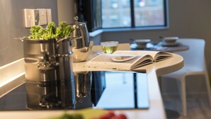 A modern kitchen with stainless steel appliances, a window with a city view, and a dining area with a table set for two. - Student Only Oldgate House (Huddersfield)