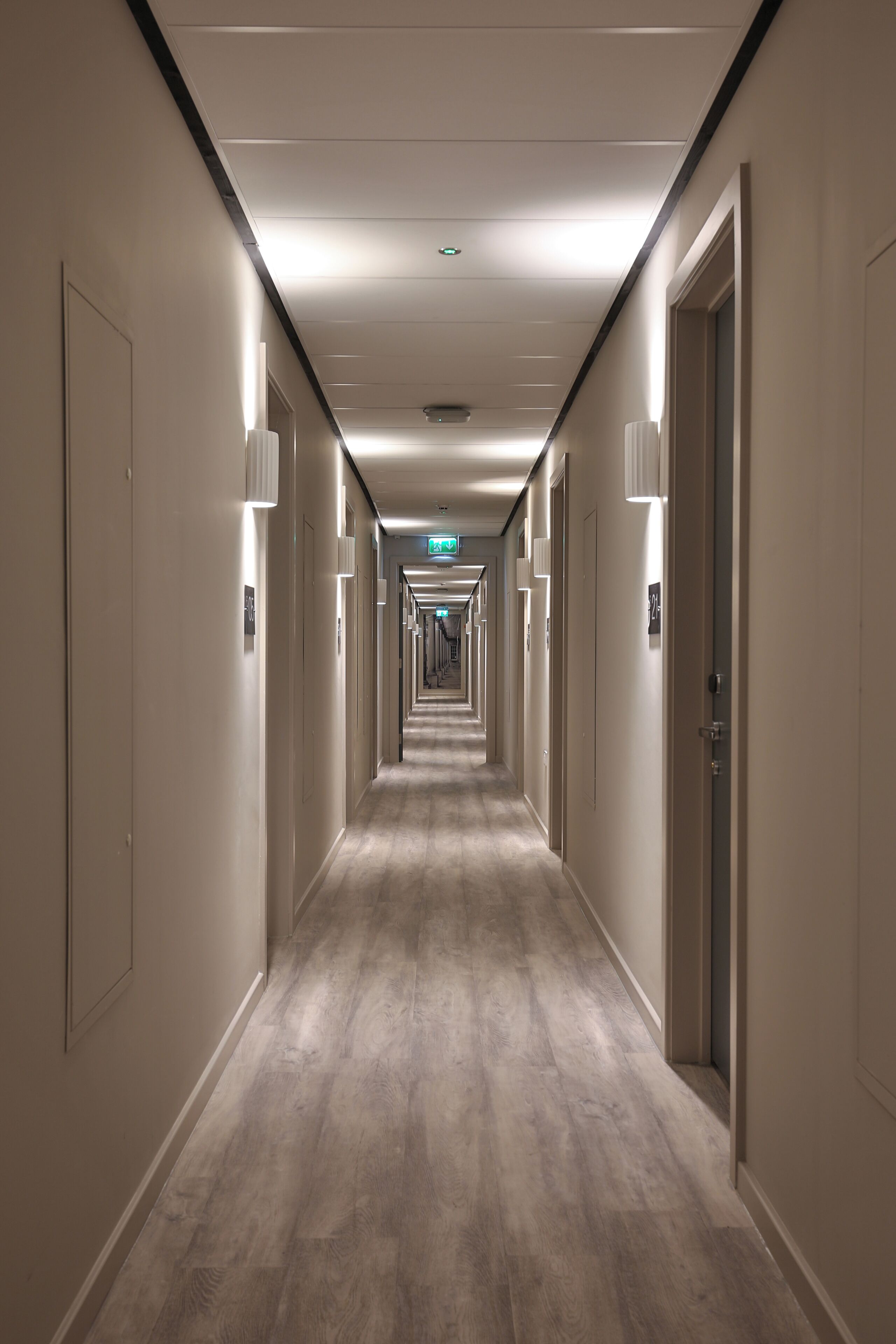 Un largo y estrecho pasillo de hotel con puertas a ambos lados, iluminado por luces del techo.
