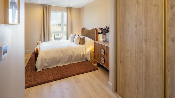 A bedroom with a bed, wooden dresser, and a view of the city. - Ocean View Aparthotel (Southampton)
