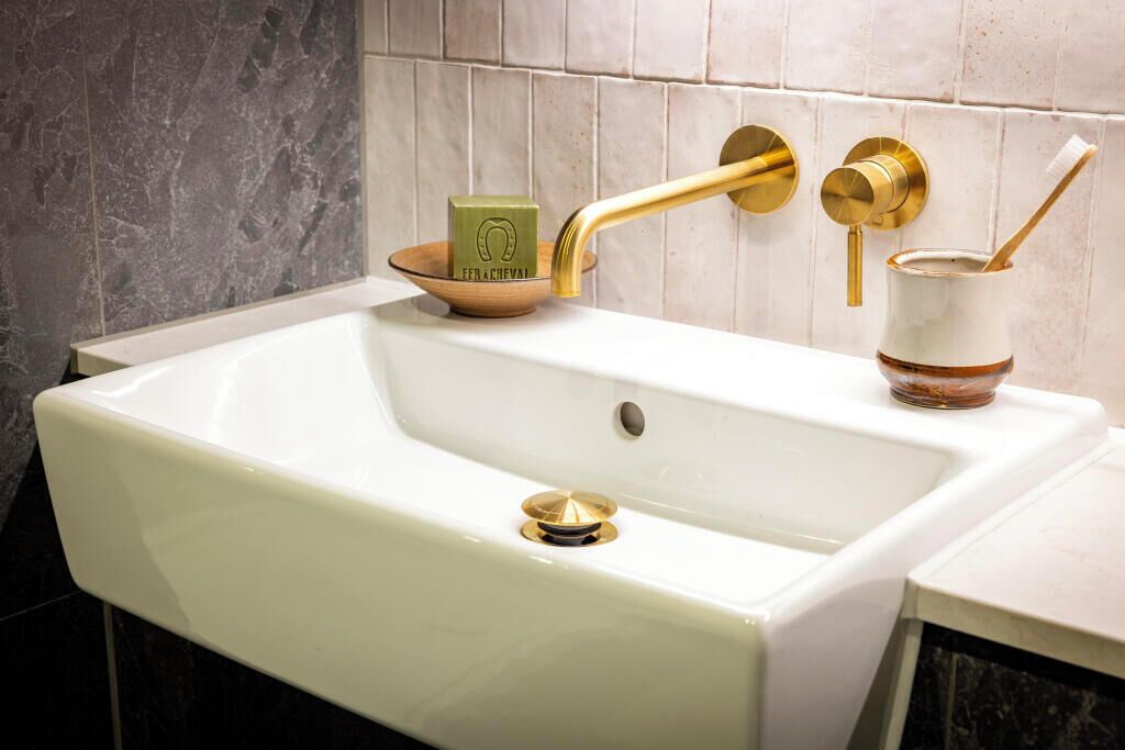A bathroom with a white sink, gold fixtures, and a soap dish.