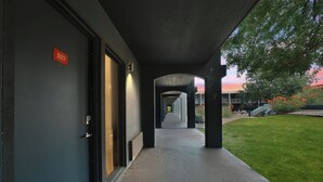 Un couloir mène à une porte portant le numéro « 503 ». Au-delà de cette porte se trouve un espace abrité d’où l’on peut admirer un coucher de soleil, ainsi qu’une zone herbeuse parsemée de fleurs.