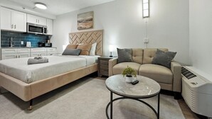 Une chambre moderne comprenant un lit, un canapé, une petite table, un radiateur et un coin cuisine.