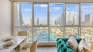 Eine hohe Wohnung mit großem Fenster und Blick auf die Stadt, einem Essbereich mit gedecktem Tisch und einem grünen, gepolsterten Sofa.