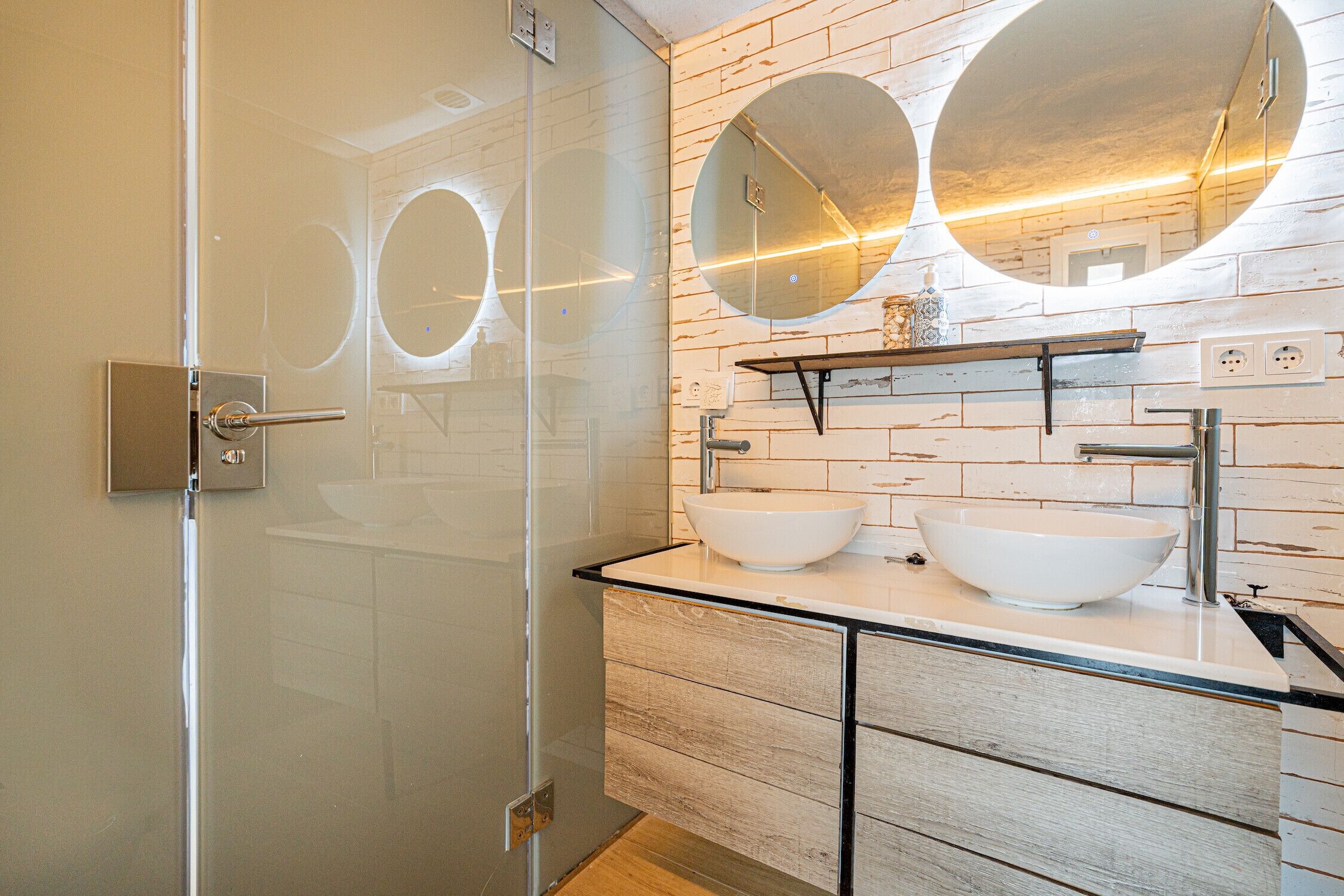 A modern bathroom with a glass shower enclosure, a white sink with a vessel basin, and a wooden vanity with drawers.