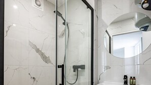 A modern bathroom with a glass-enclosed shower, marble tiles, a wooden vanity with drawers, and a mirror above the sink.