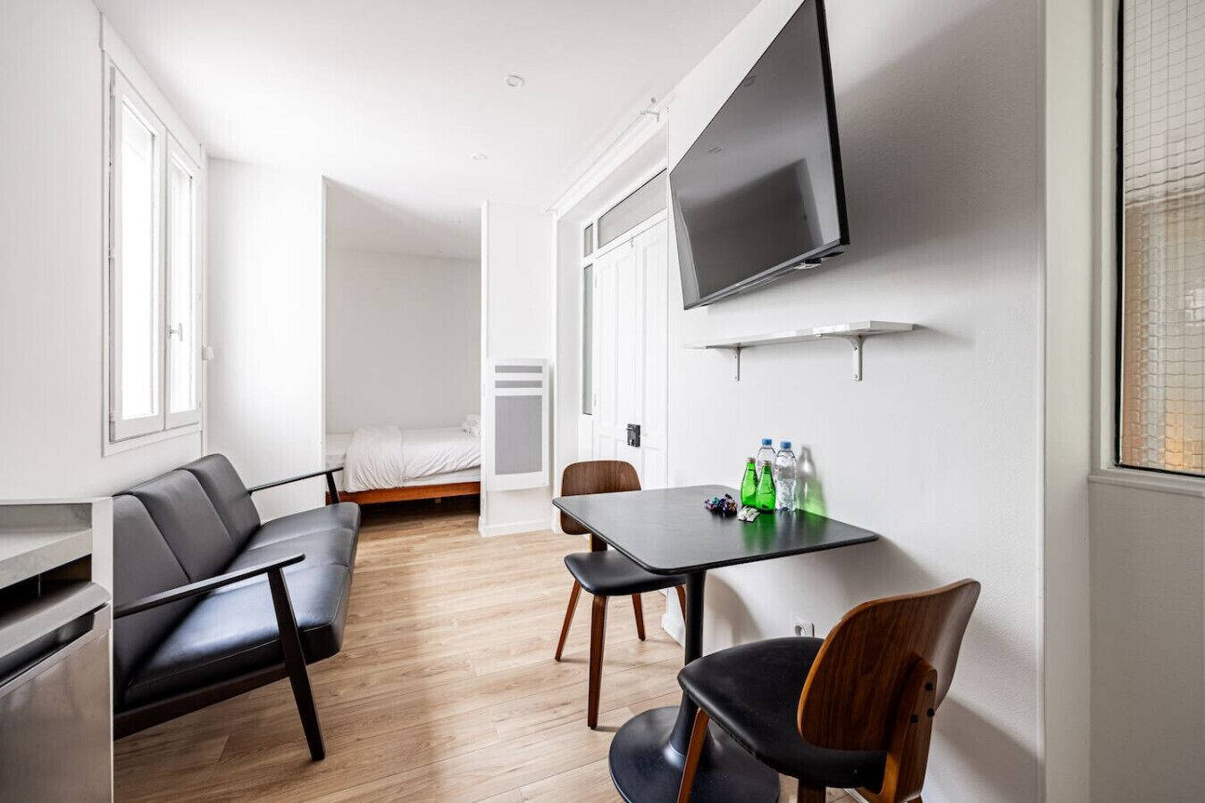 A modern, well-lit room with a bed, a TV mounted on the wall, a table with chairs, and a sofa.
