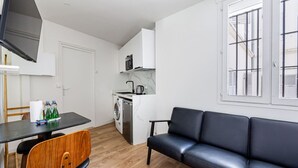 A compact living space with a kitchenette, a washing machine, a sofa, and a dining area.