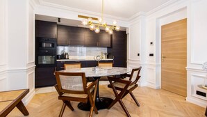 A modern kitchen with dark cabinets, a marble countertop, and a dining area with a round table and chairs. - #3Bedrooms#Lafayette#Paris10#AC (Paris)