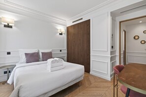 A hotel room with a bed, bedside lamps, a wooden wardrobe, a round table, and a chair.