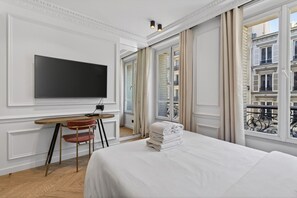 A hotel room with a bed, a desk, a chair, a television, and a window with a view of buildings.