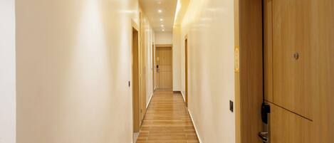 A long, narrow hallway with wooden doors on one side and a tiled floor.