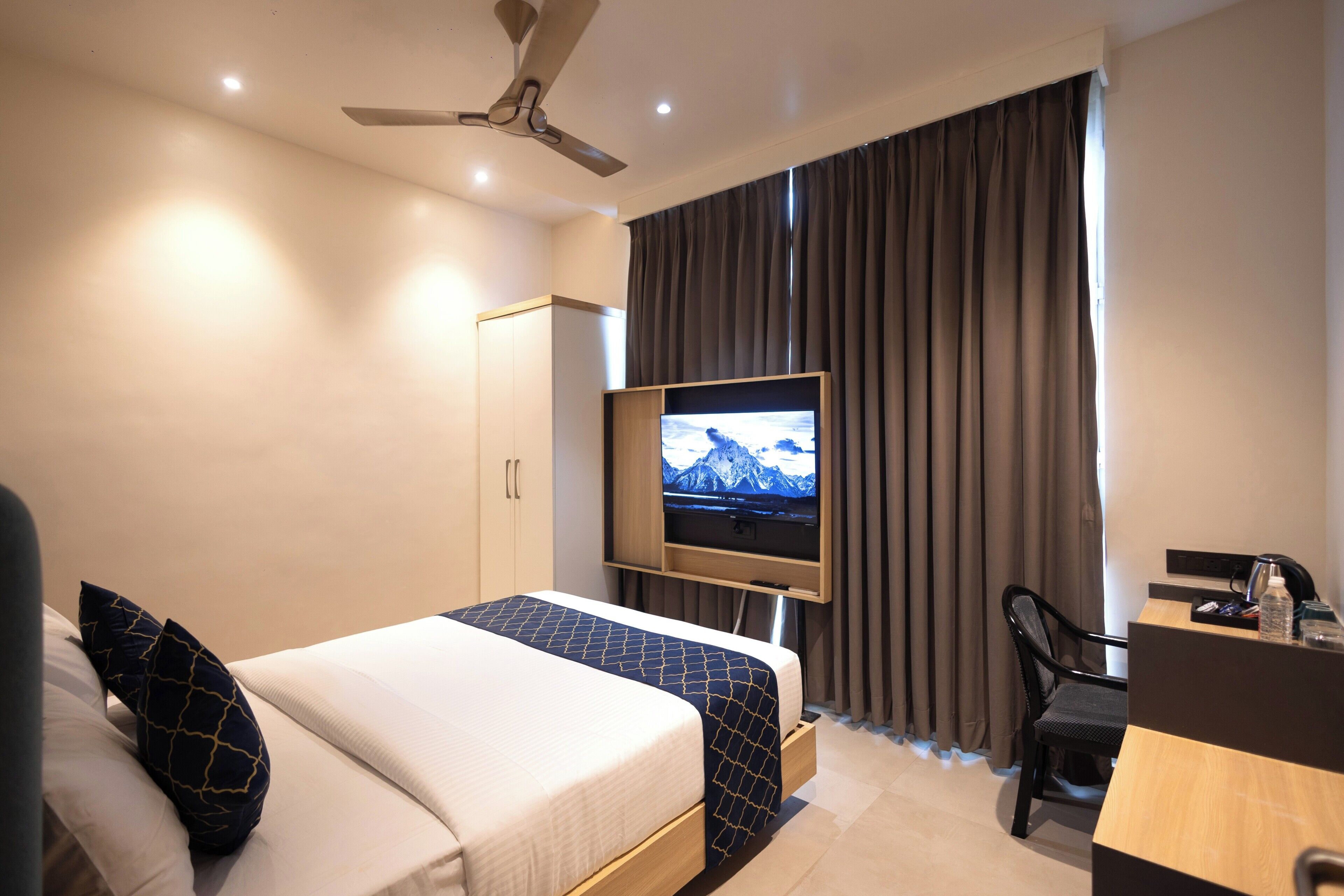 Een hotelkamer met een bed, een bureau, een televisietoestel en een plafondventilator.