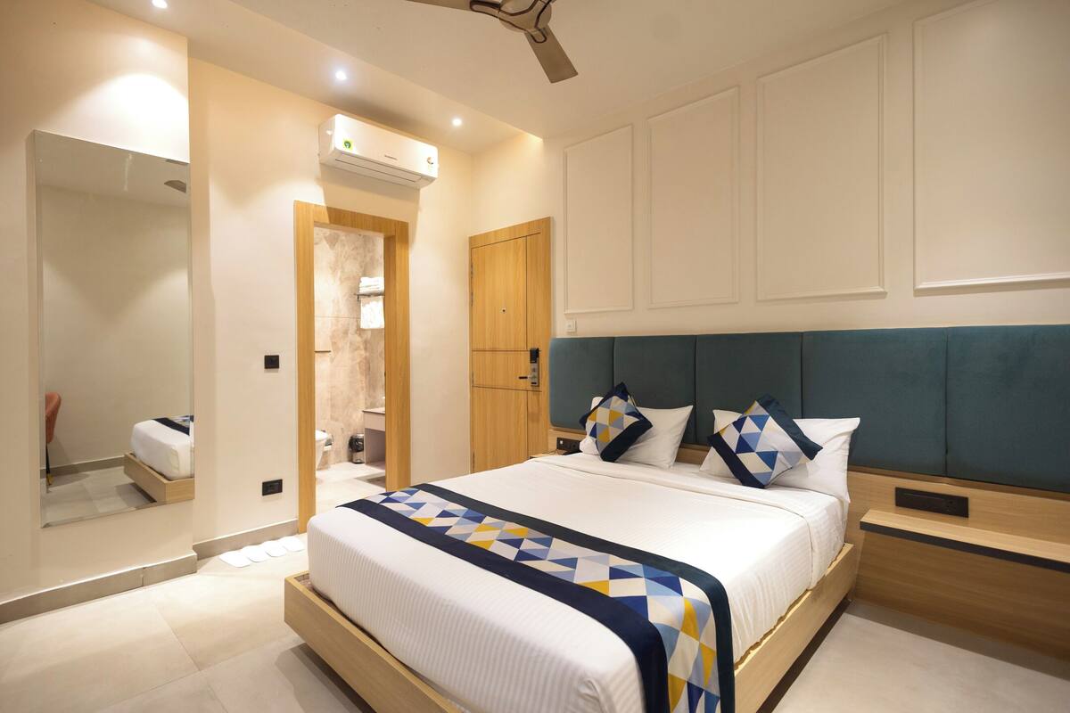 A modern hotel room with a large bed, a wooden headboard, a built-in wardrobe, and a mirror.