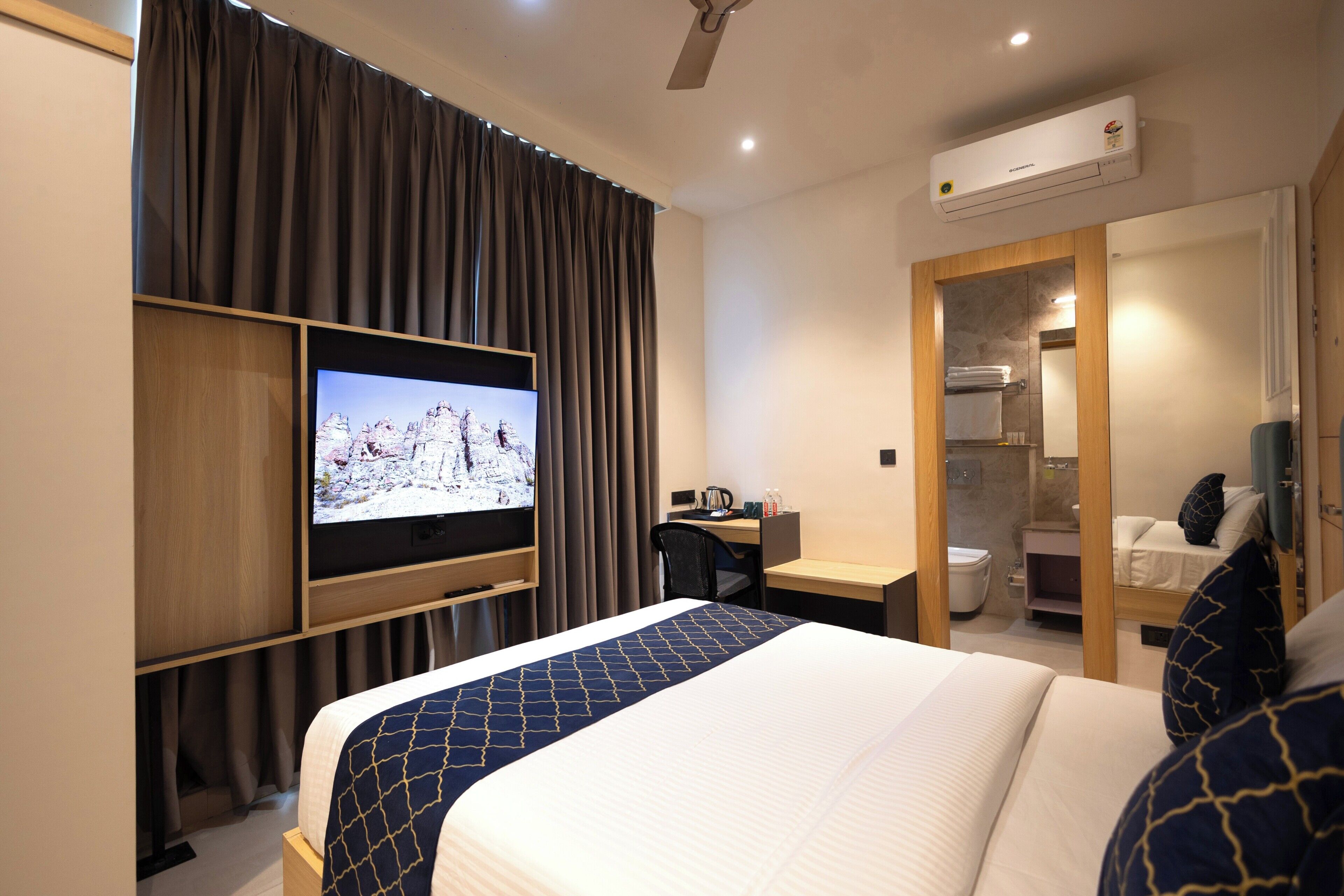 Habitación de hotel con cama, televisor, escritorio y baño visible a través de una puerta abierta.