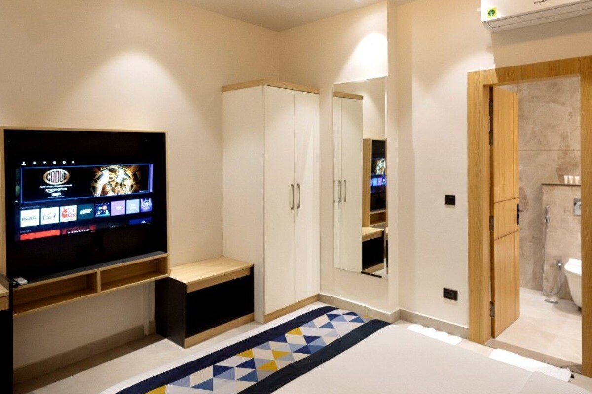 A modern bedroom with a bed, a TV, a ceiling fan, and a bathroom visible through an open door.