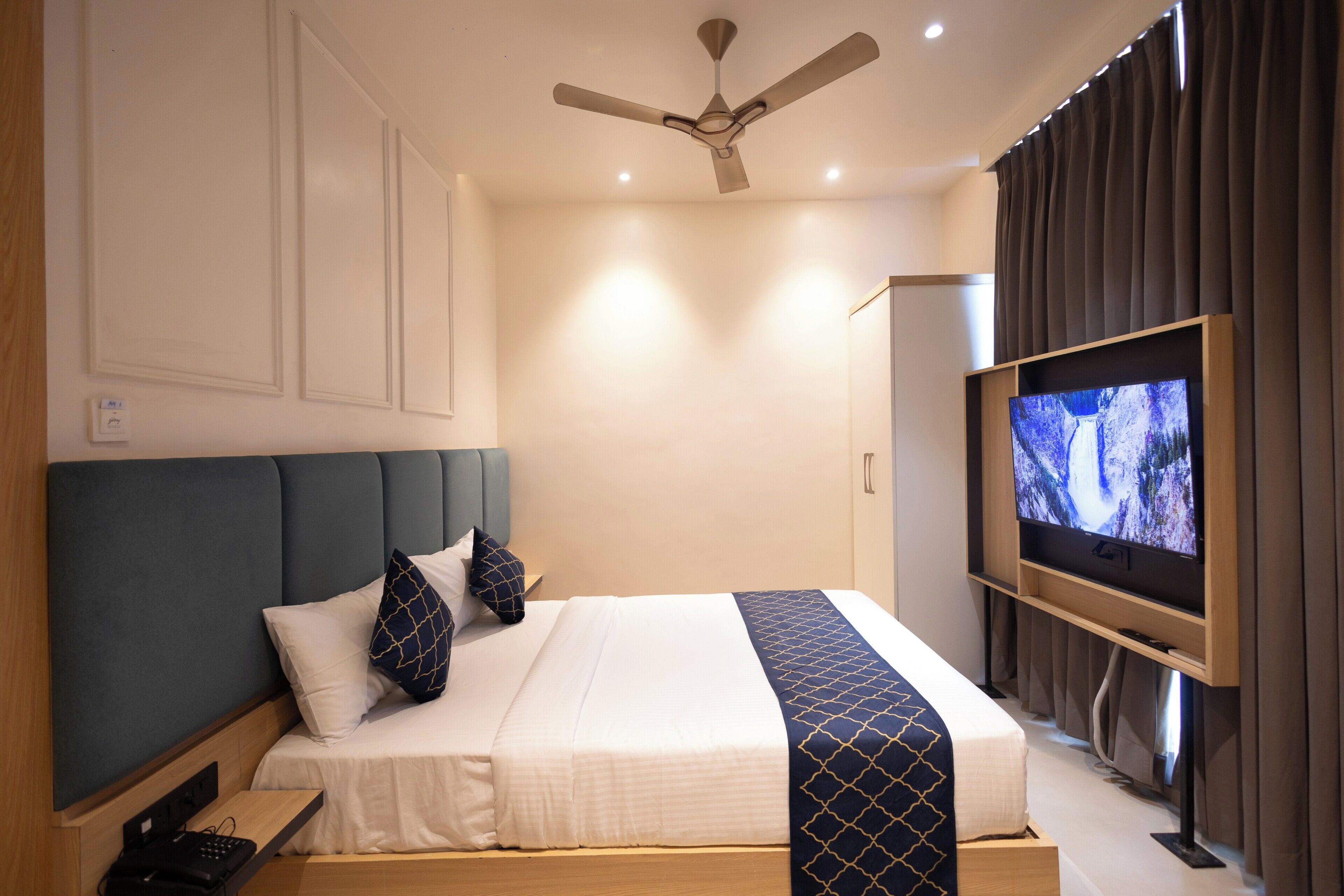 A hotel room with a bed, a ceiling fan, a TV, and a wardrobe.
