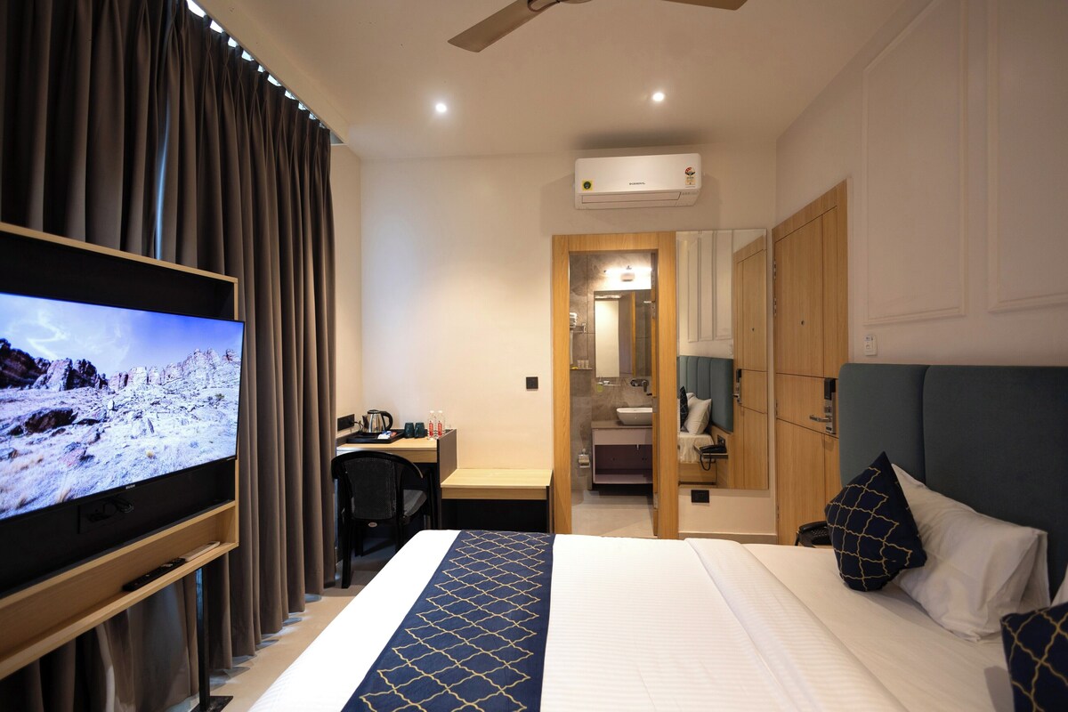 A hotel room with a bed, a desk, a television, and a bathroom visible through an open door.