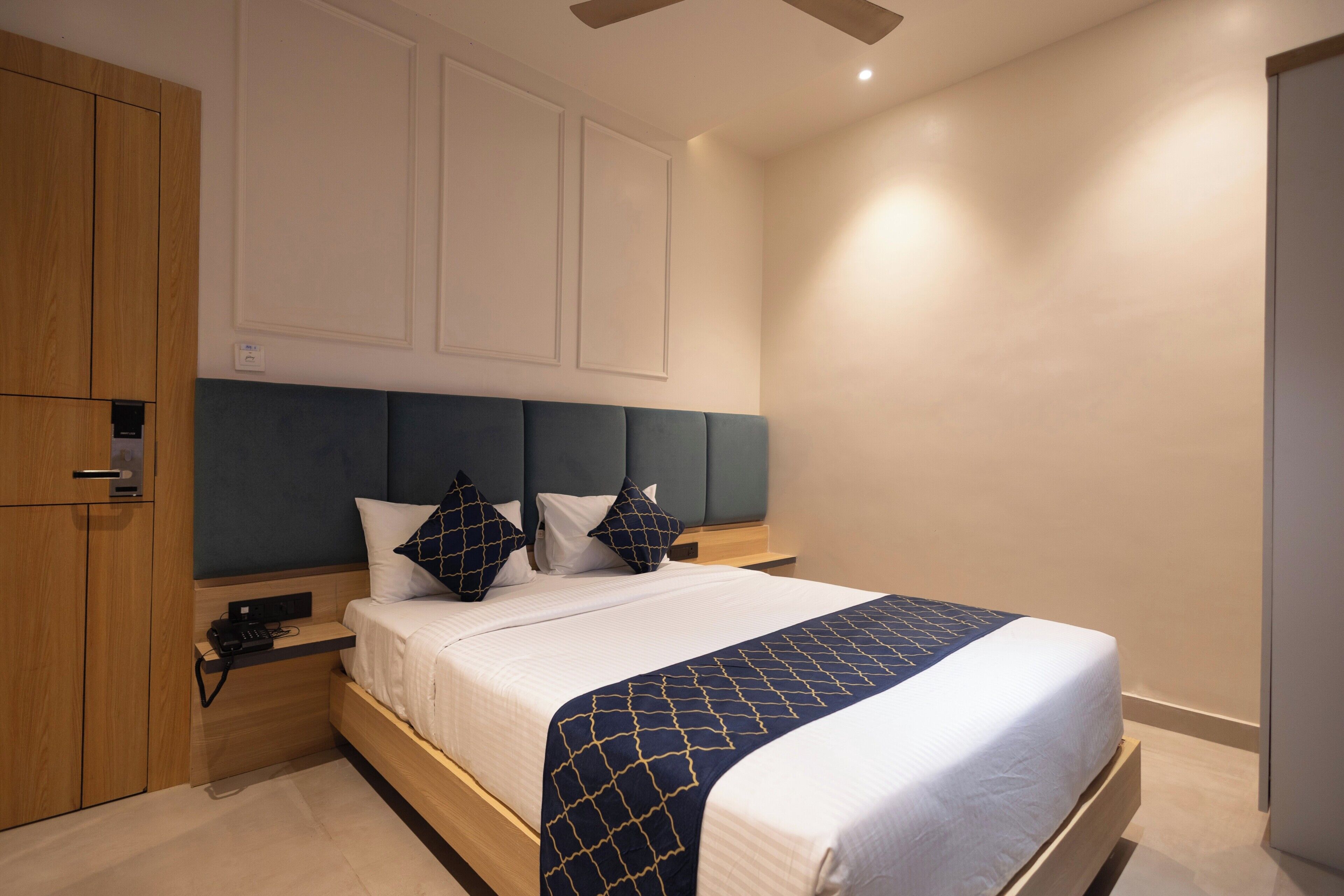 A modern hotel room with a bed, wooden wardrobe, bedside table, and a nightstand.