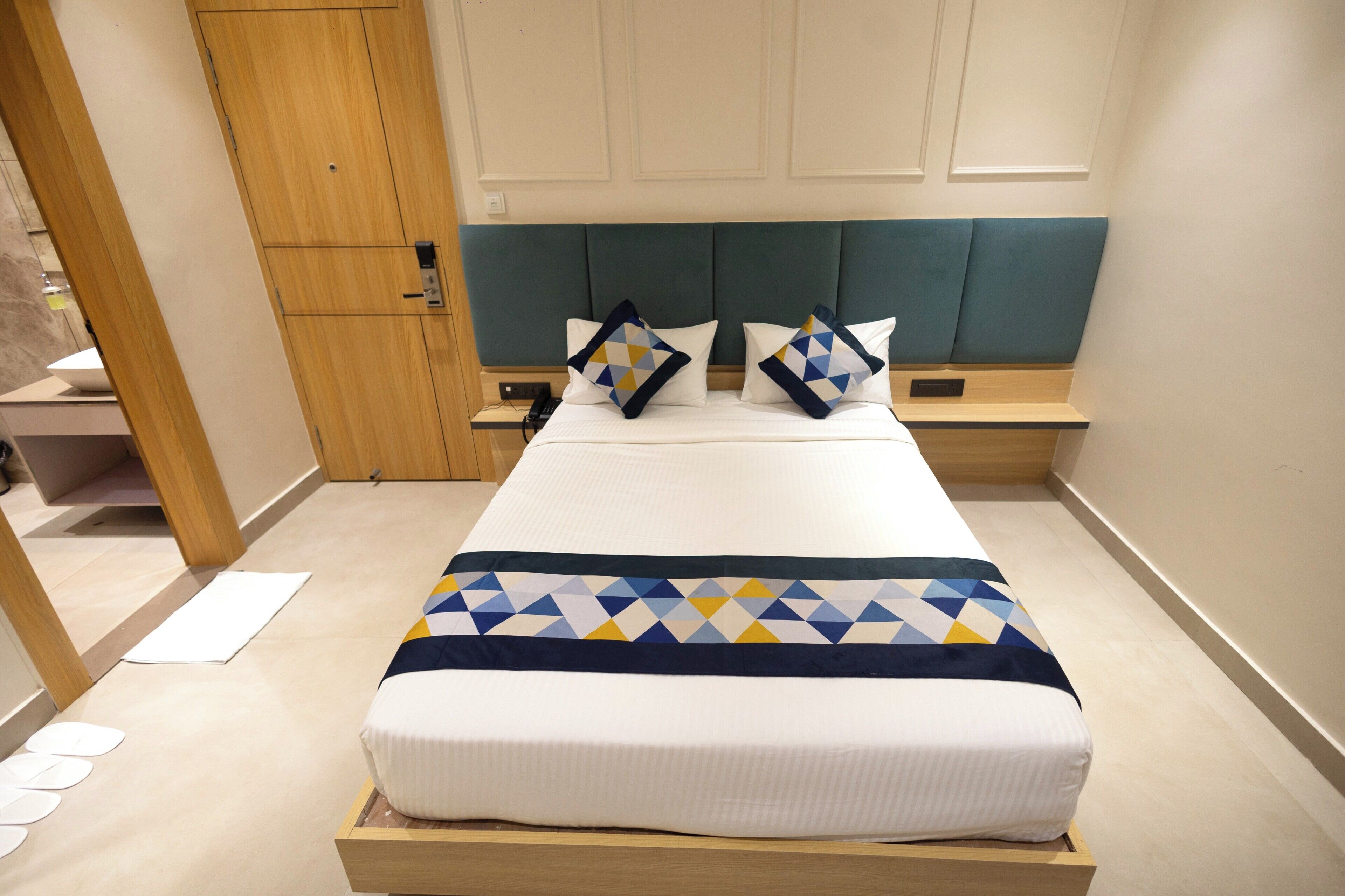 A neatly made bed with a geometric-patterned blanket, a wooden headboard, and two bedside tables with lamps.