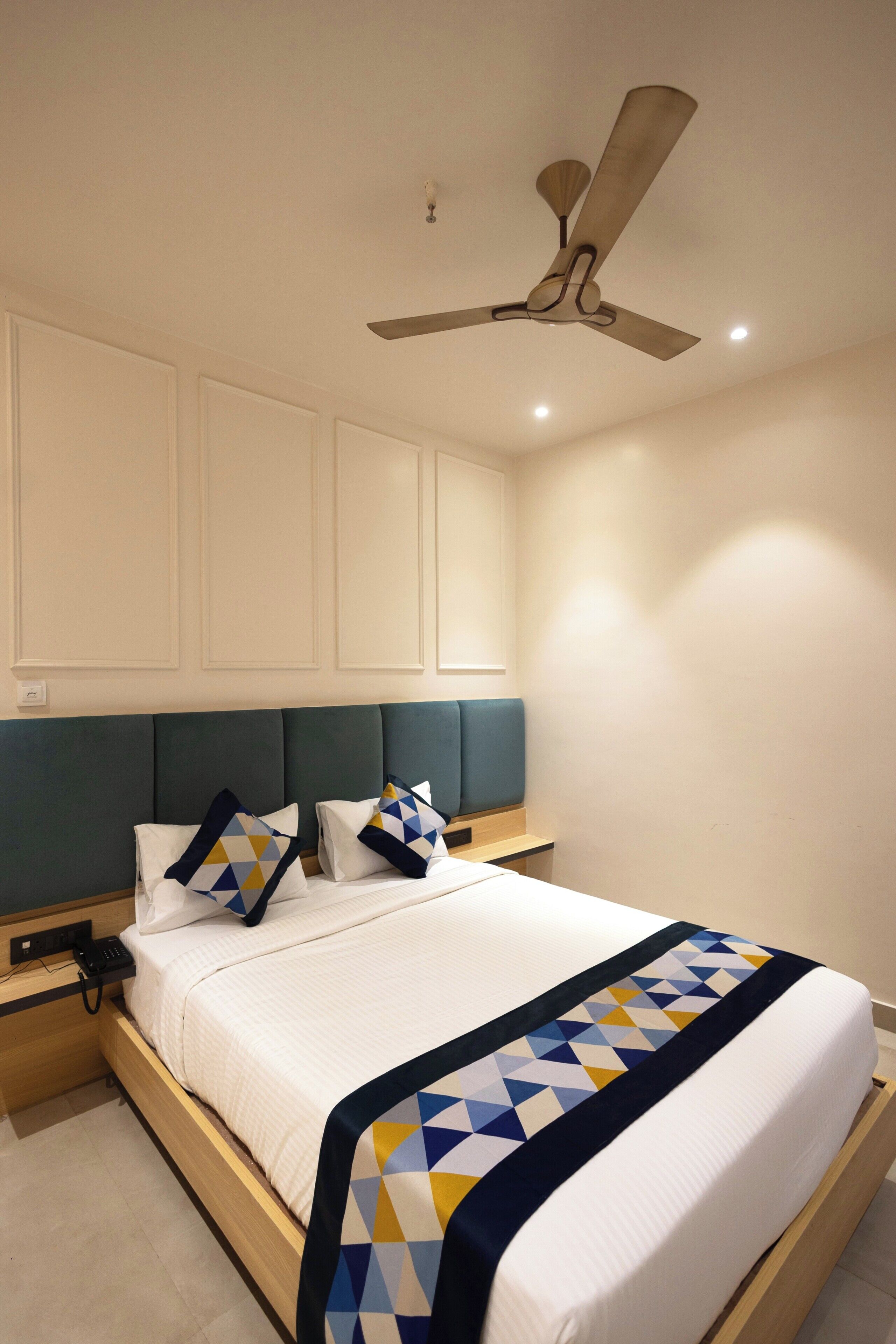 A neatly made bed with a geometric-patterned blanket, a ceiling fan, and a bedside table with a phone.