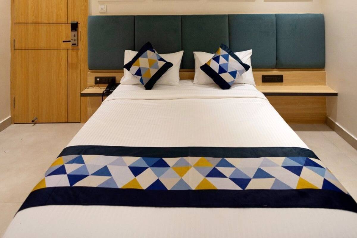 A hotel room with a bed, a ceiling fan, a wooden wardrobe, and a green upholstered headboard.