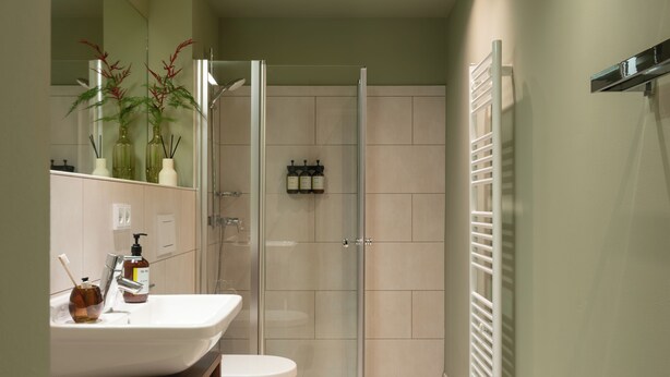 Ein Badezimmer mit Duschkabine aus Glas, einem weißen Waschbecken mit Spiegel und einer Toilette.