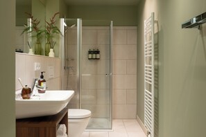 A bathroom with a glass shower enclosure, a white sink with a mirror, and a toilet. - Bob W Munich City West (Munich)